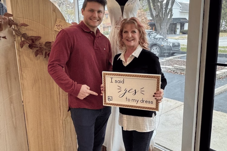 Bride and companion holding an "I said yes to my dress" sign inside a bridal boutique after finding her wedding dress