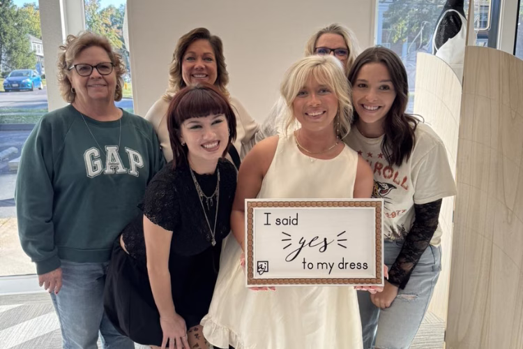 Bride-to-be holding a “I said yes to my dress” sign while celebrating with family and friends after finding her wedding dress at a bridal boutique.