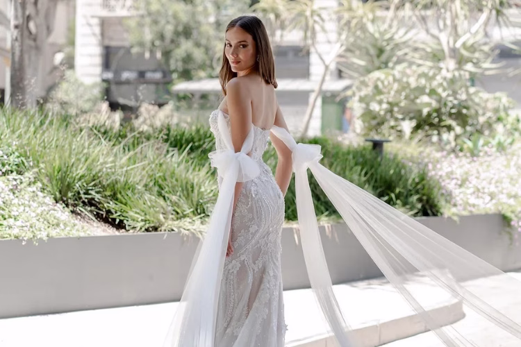 Bride wearing a contemporary fitted wedding dress with statement bow details and flowing tulle accents in an urban setting.