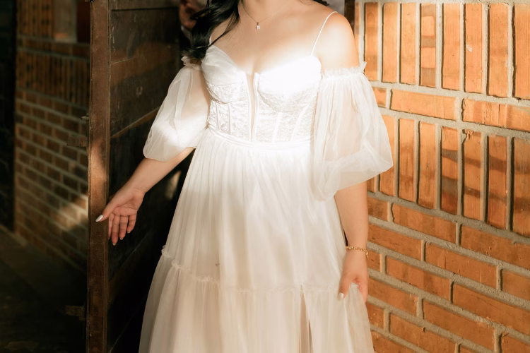 Bride wearing a flowy off-the-shoulder wedding dress with sheer sleeves, suited for a rustic barn wedding setting.
