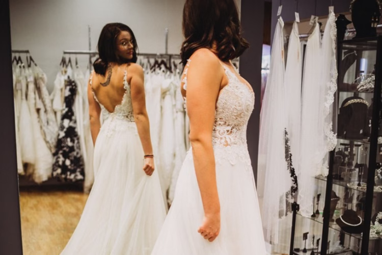 Bride trying on a lace wedding dress and looking at her reflection in a mirror during a bridal gown shopping appointment.