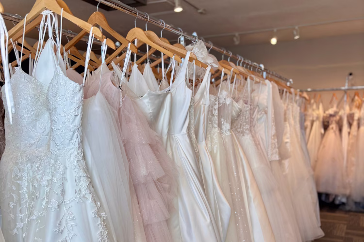Wedding dresses displayed on racks in a bridal boutique, featuring a variety of lace, satin, and tulle bridal gowns.