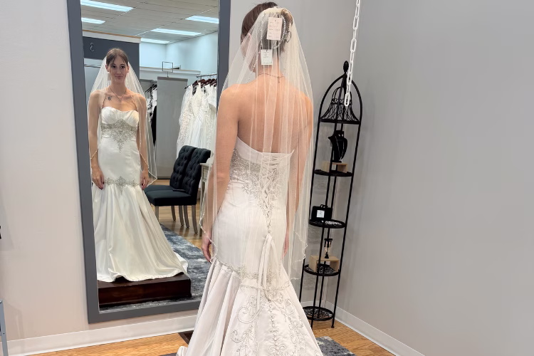 Bride trying on a fitted wedding dress with a veil during a bridal appointment in a boutique fitting room.