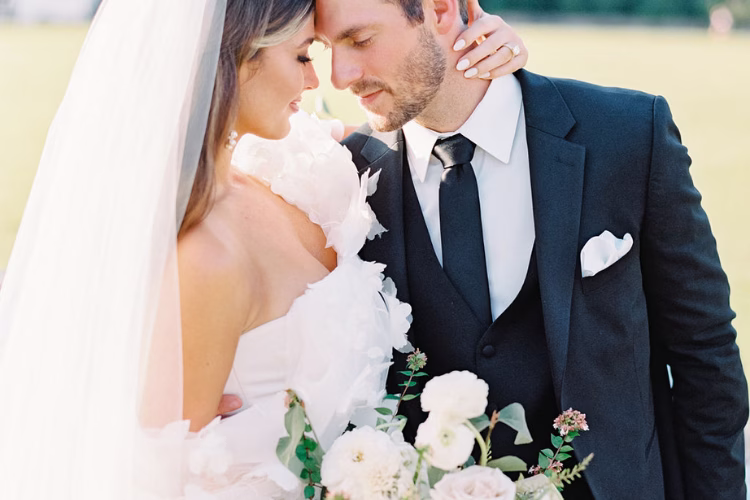 Bride and groom embracing outdoors, with the groom wearing a dark navy suit, white shirt, and matching tie.