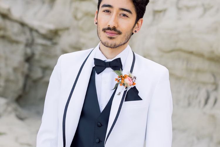 Groom wearing a white tuxedo jacket with black trim, black vest, and bow tie, accented with a floral boutonniere.