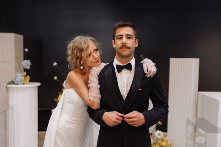 Bride standing beside her groom, who is wearing a black tuxedo, black bow tie, and white pocket square.