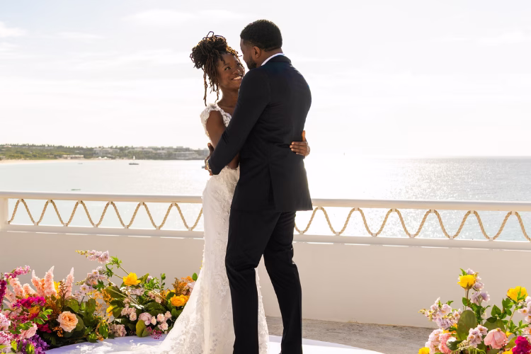Bride and groom embrace on a seaside wedding terrace overlooking the water.