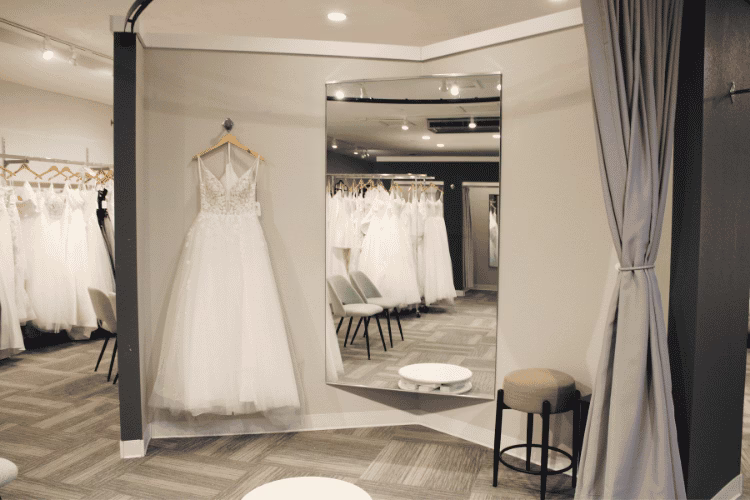 Wedding dress displayed beside a large mirror in a bridal boutique fitting area