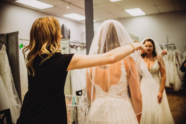Bridal consultant adjusting a bride's veil and wedding gown in a bridal boutique