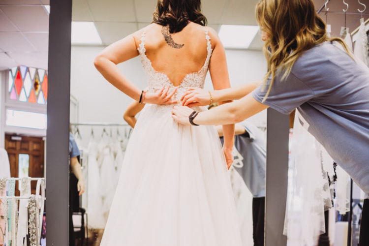 Bridal consultants adjusting the back of a bride's wedding gown during a fitting