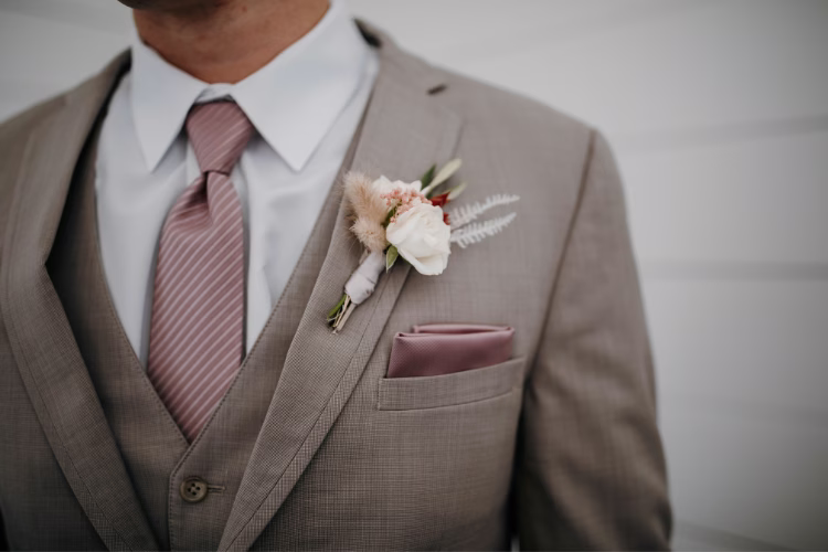 Close-up of a man wearing a taupe suit with a vest, pink tie, pocket square, and floral boutonniere.