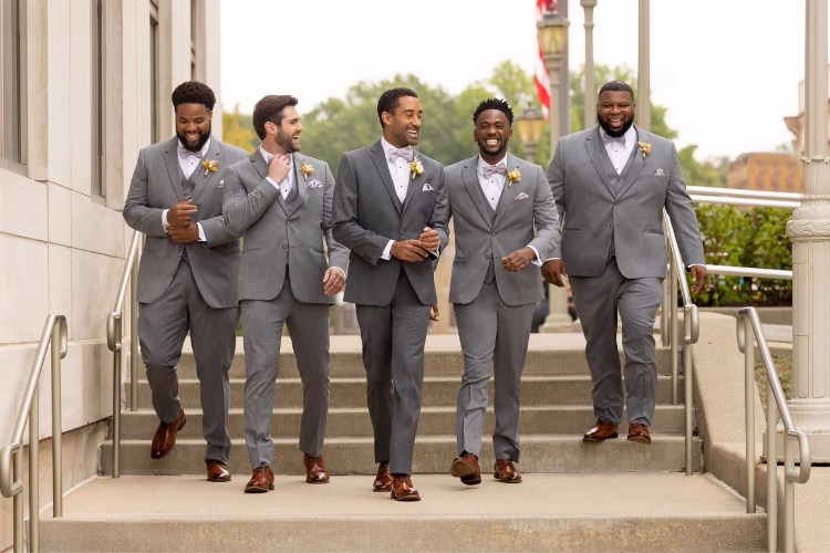 Groom and groomsmen walking down outdoor steps in coordinated gray suits with matching boutonnieres.