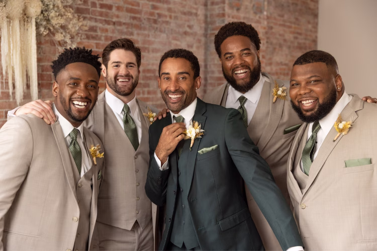 Groom and groomsmen smiling together in coordinated beige and dark green suits with floral boutonnieres.